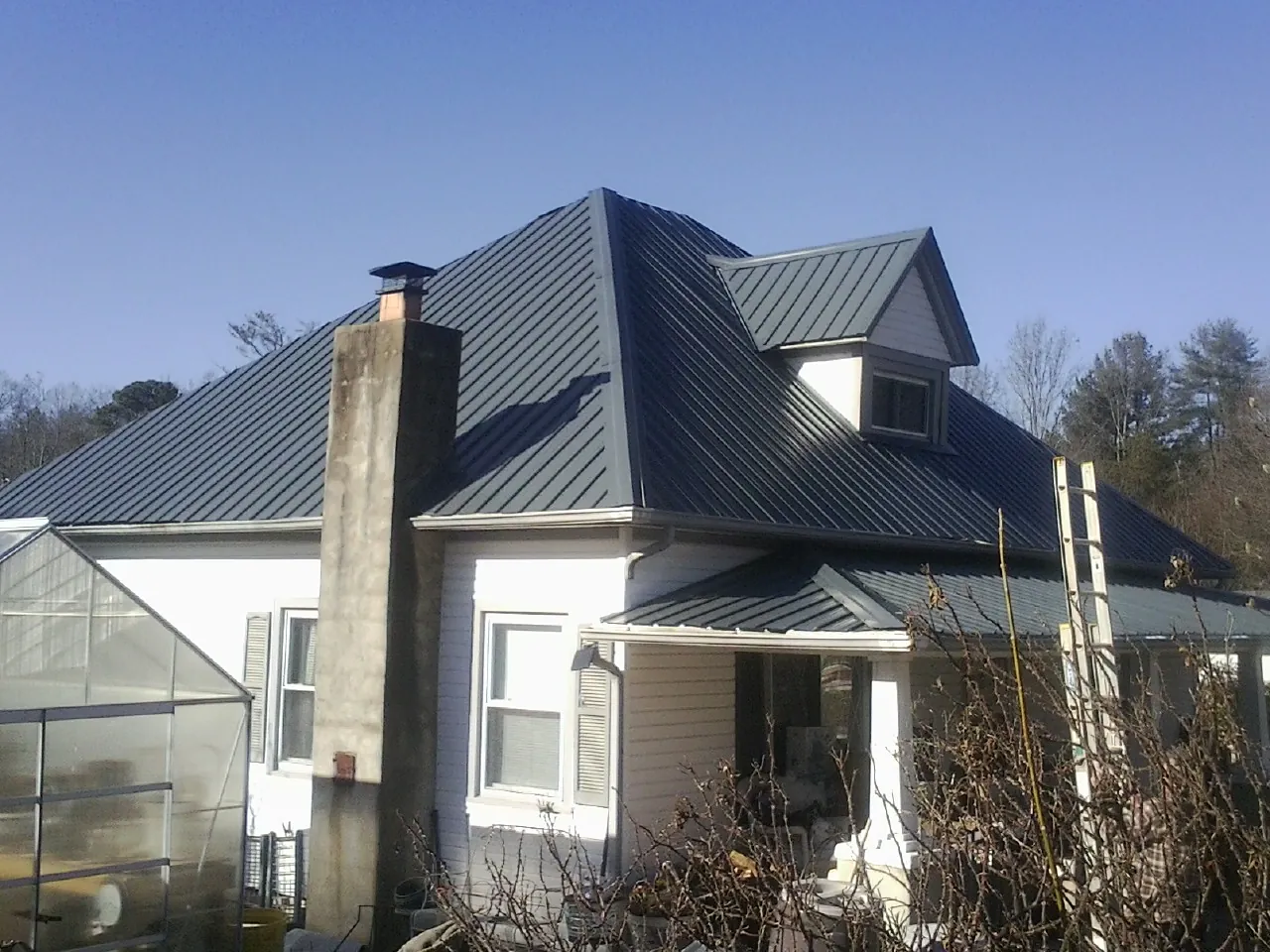 Dark blue standing seam metal roof on a white farmhouse with dormer — Slate & Tile Roof Repair by Roofing Brothers in Clairton