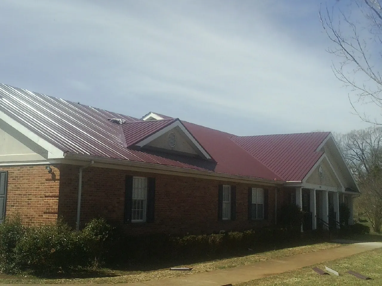 Red metal roof with gabled entries on a long brick building, from a Hail Damage Roof Repair job in Clairton