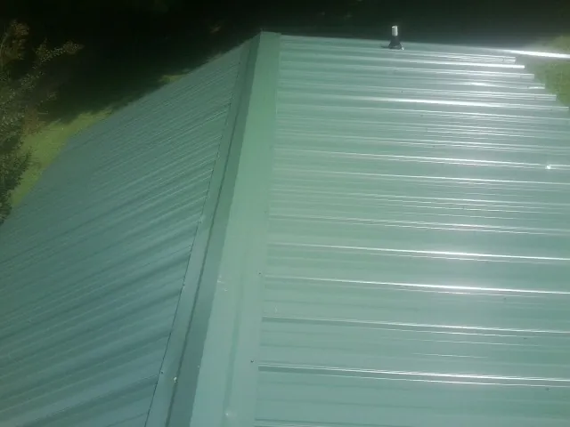 New green metal panels meeting at the ridge of a roof — Flat Roof Repair work by our crew in Clairton