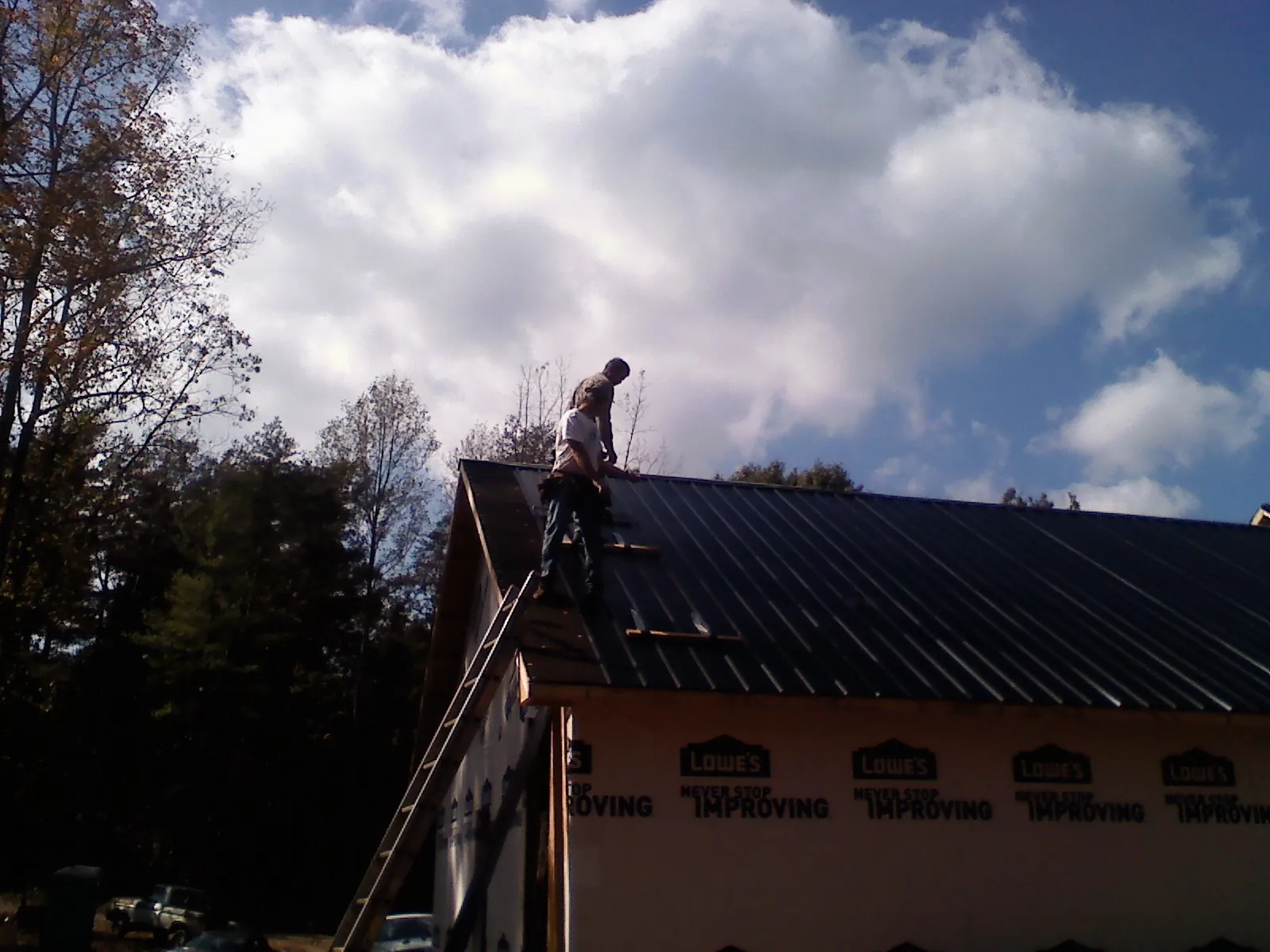 Roofer fastening dark metal panels high against a cloudy sky, from a Roof Inspection job in Clairton