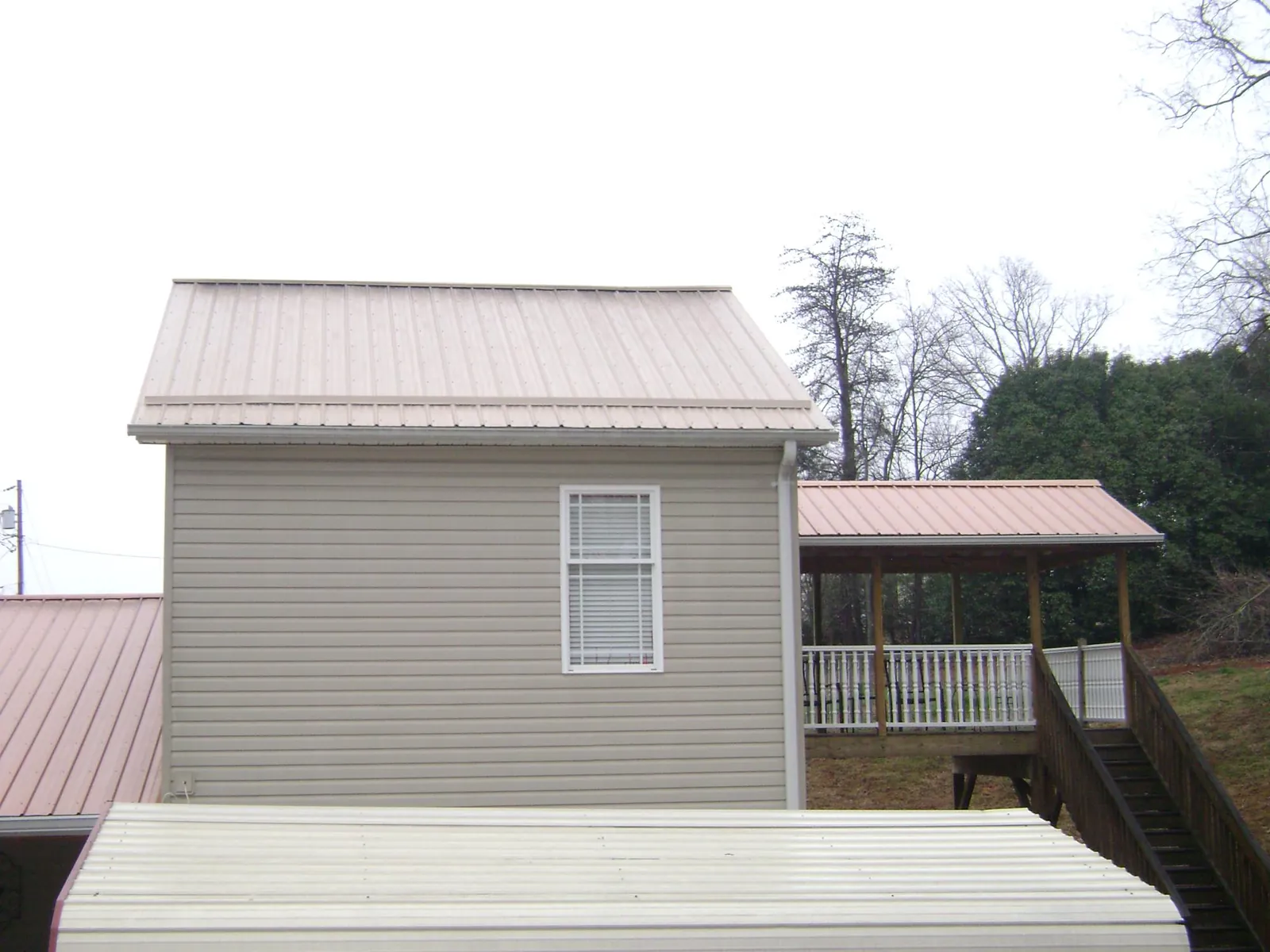 Tan metal roofs on a two story addition and attached porch, from a Roof Replacement job in Clairton